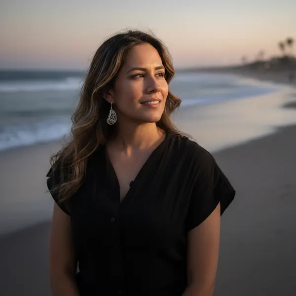 Model in black at dusk on the beach wearing drop earrings, waves in soft focus