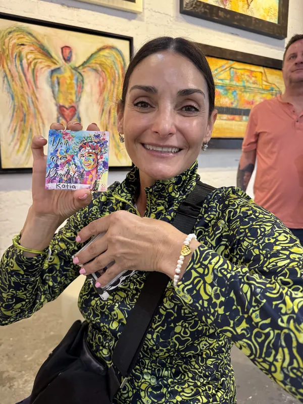 Beaming client at the gallery holding up her hand-painted MIA ceramic personalized with her name, Katia